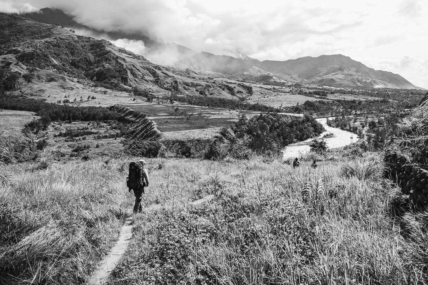 backpacker walking in grass field with river