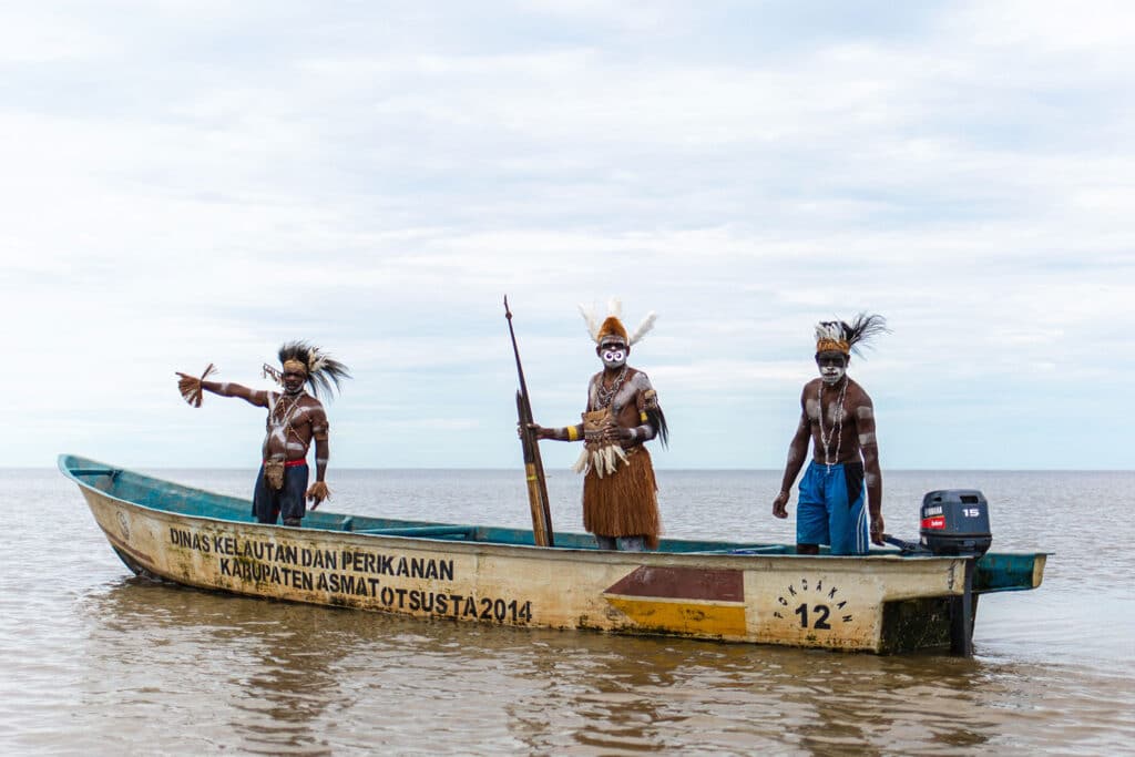 three decorated Asmat tribe men standing in a boat