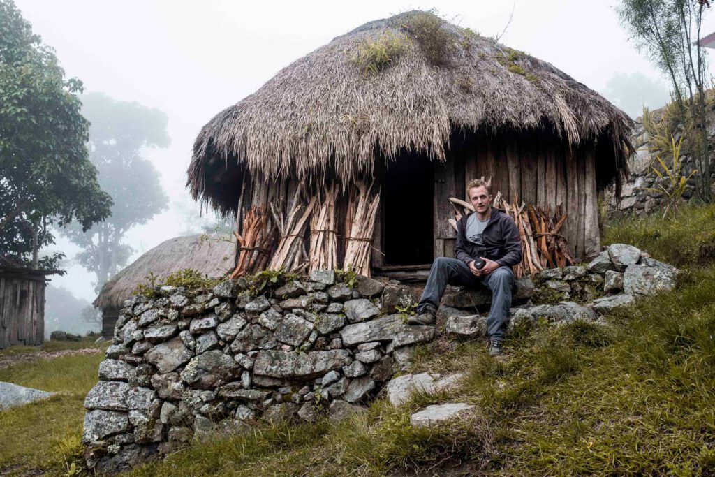 Mann, der vor einem traditionellen Haus im Baliem-Tal in Papua sitzt