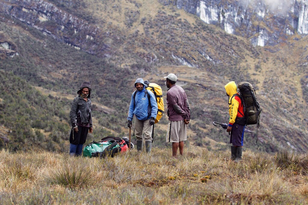 Papua vier Träger machen Pause mit Berg im Hintergrund