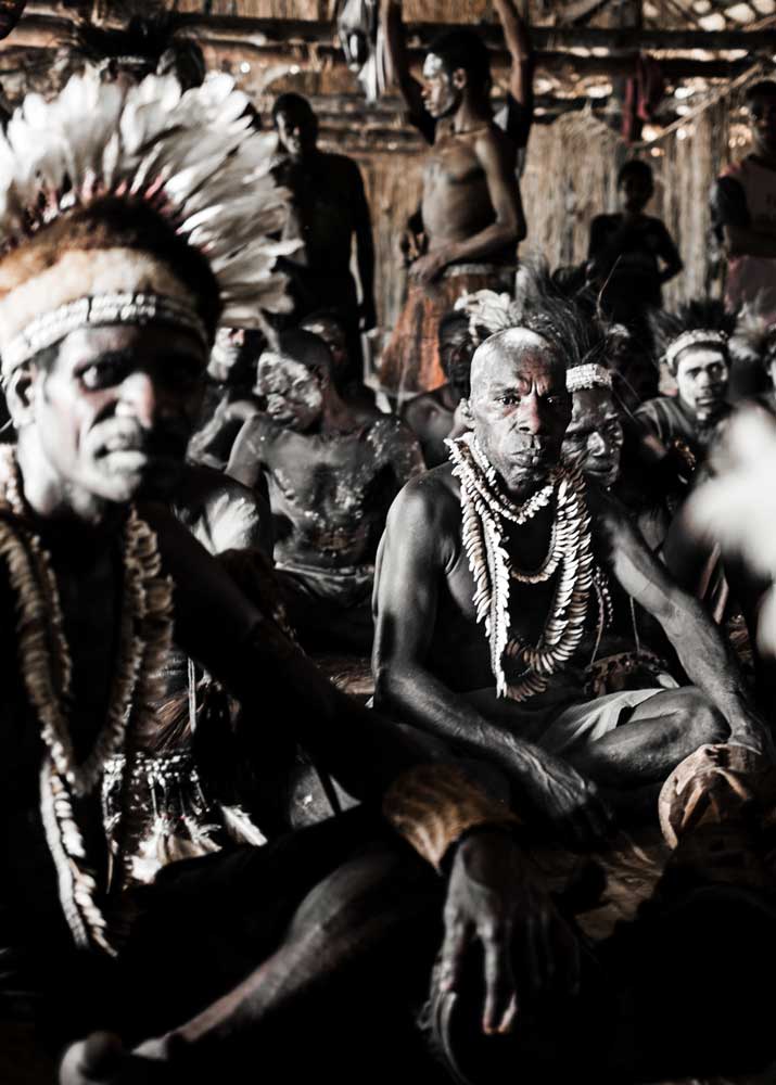 group of Asmat men with feather decoration sitting in a traditional house